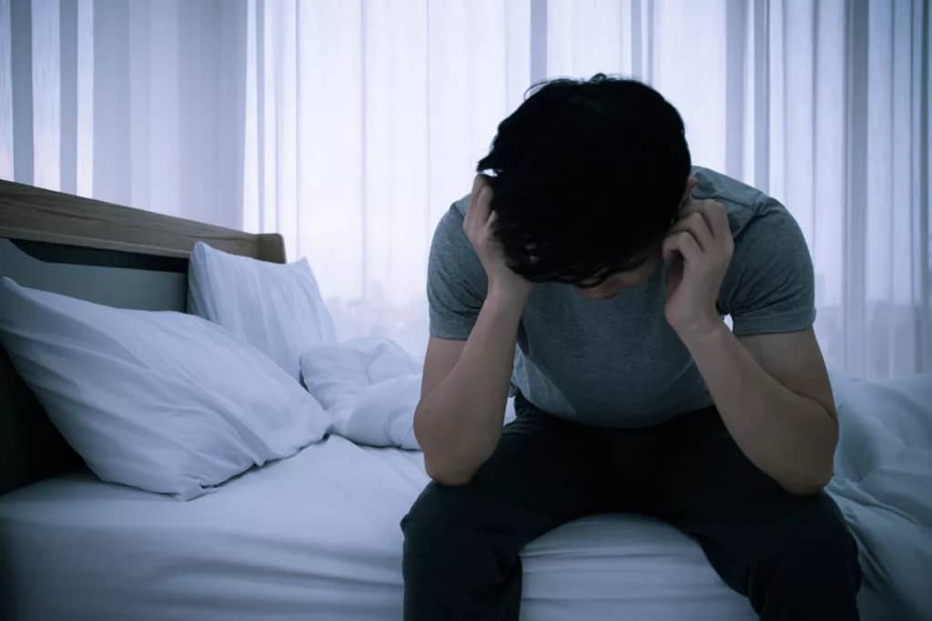 Stressed Asian young man sitting alone on bed. Bad relationship or bankrupt problem and sickness concept.